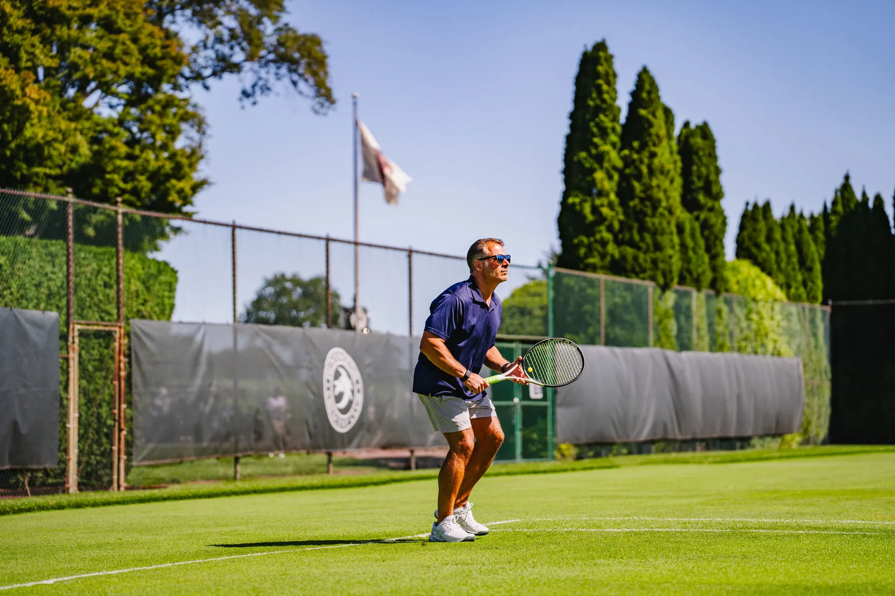 Tennis player on the grass court with club crest in background
