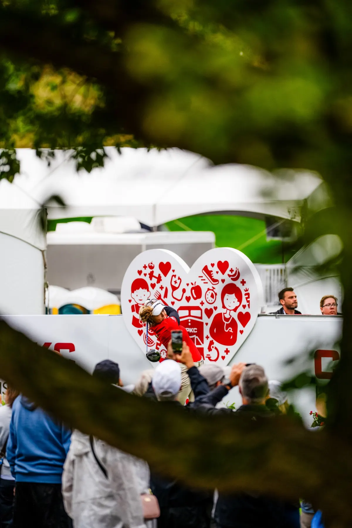 A tee shot framed by trees in front of a heart-shaped CPKC sign