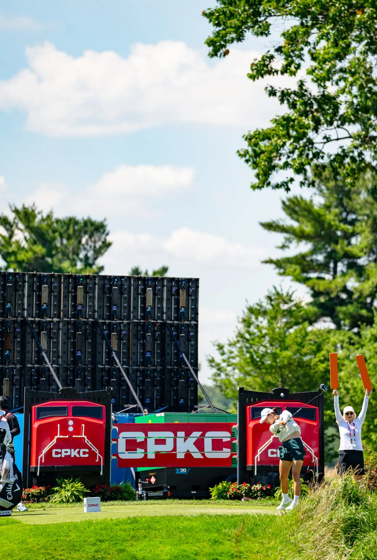 A tee shot between CPKC locomotive signs as a marshal raises paddles