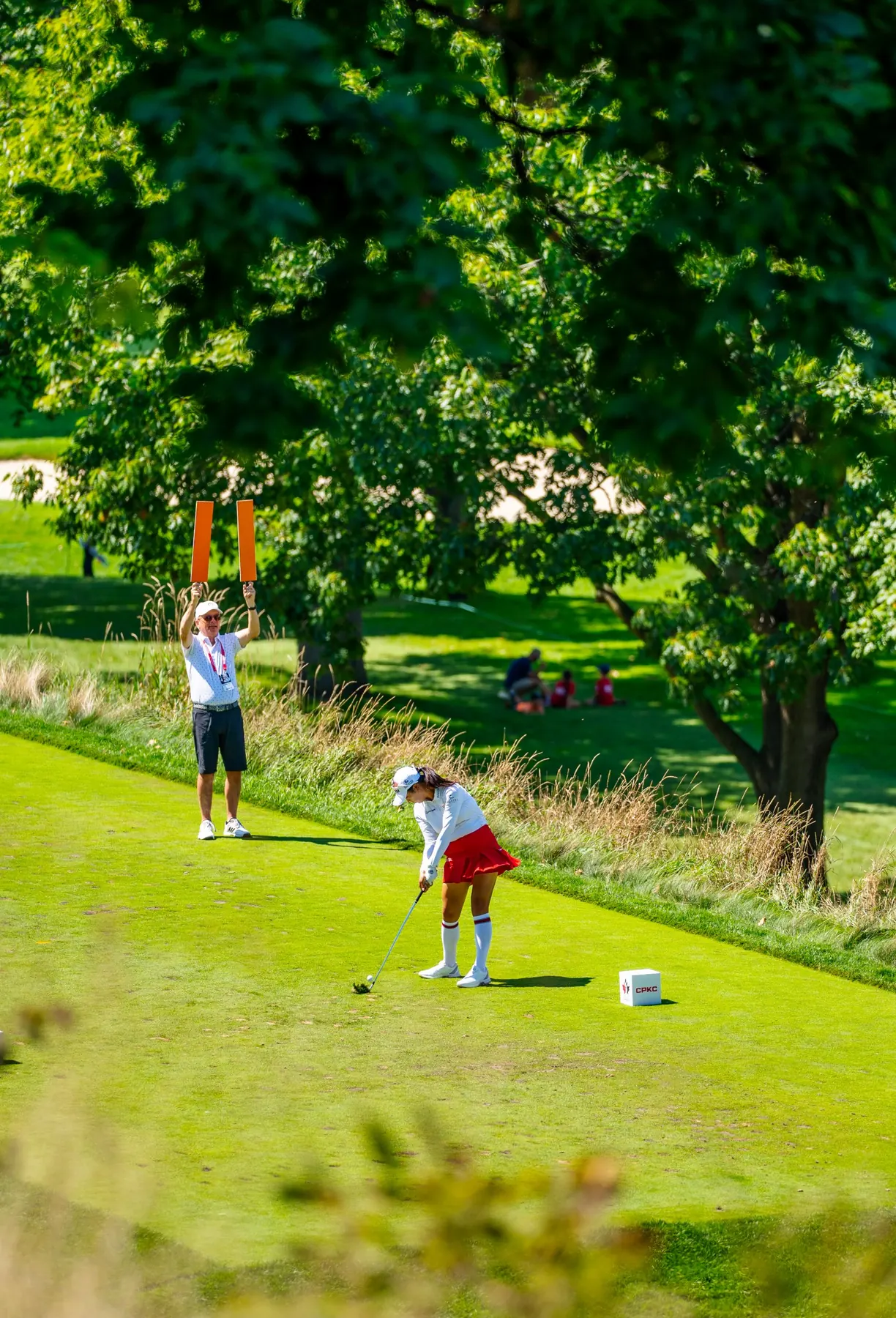 A player tees off as a marshal raises paddles behind her