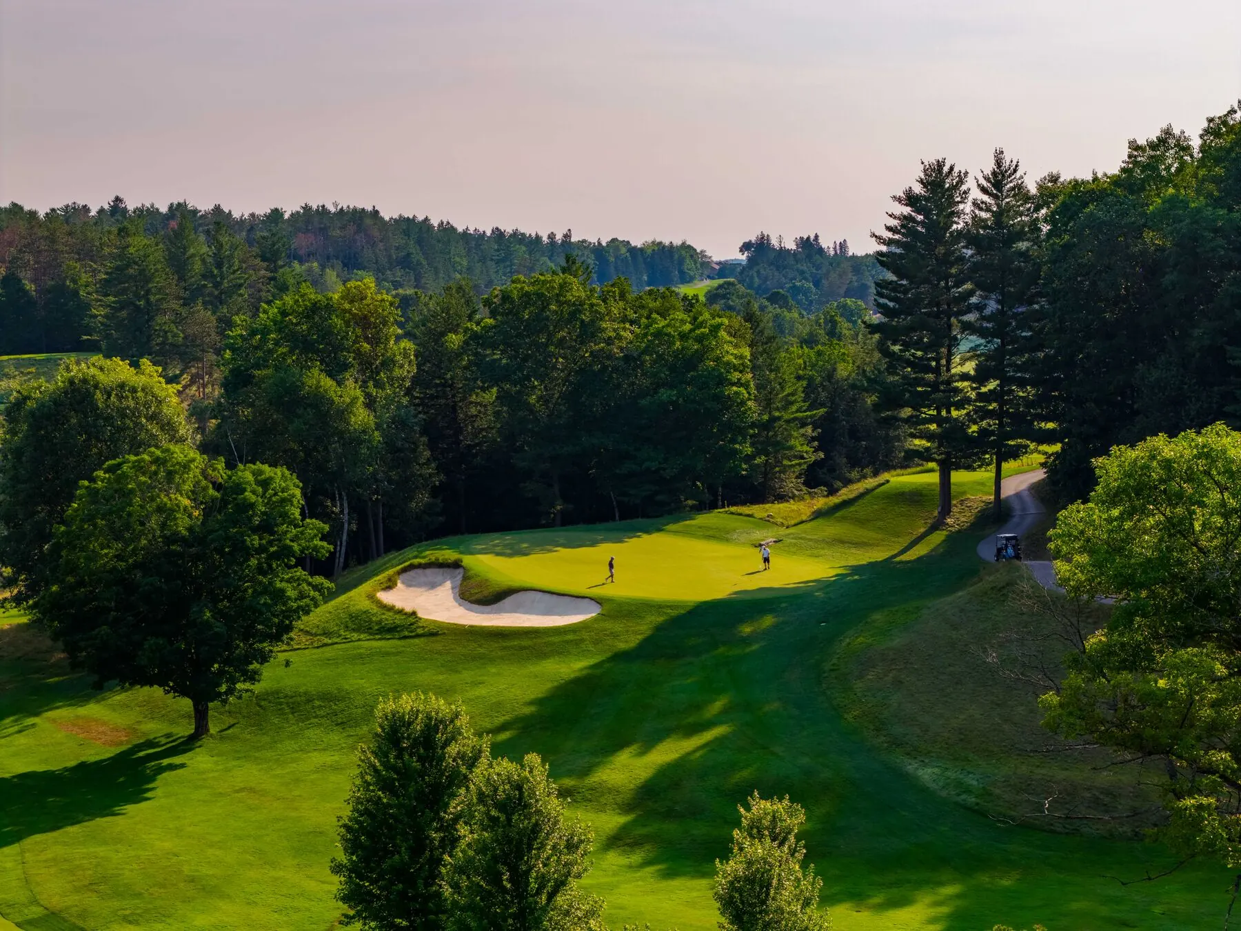 Golfers on the green with bunker and cart path